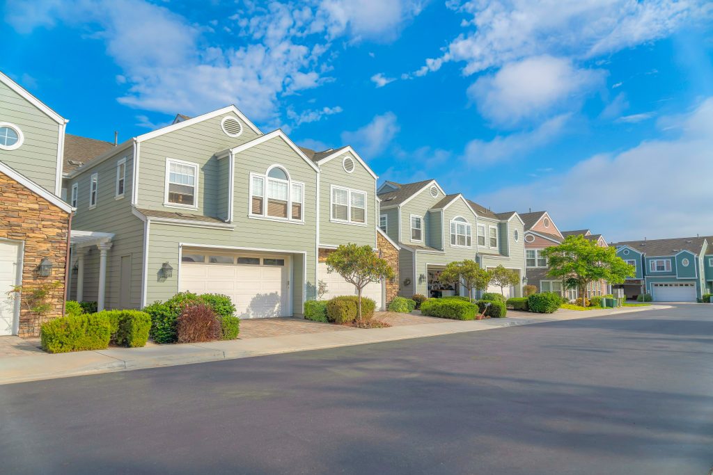Duplex houses with green wood vinyl sidings at Carlsbad, San Diego, California. There are white garage doors with concrete driveway near the plants at the front.