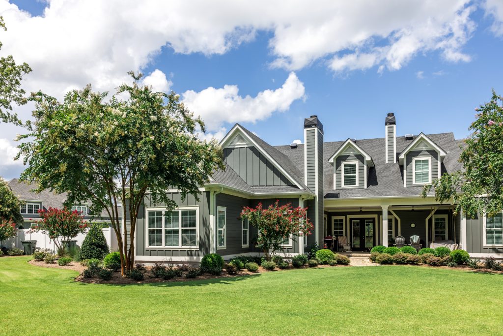 The side view of a large gray craftsman new construction house with a landscaped yard and a garage and driveway.