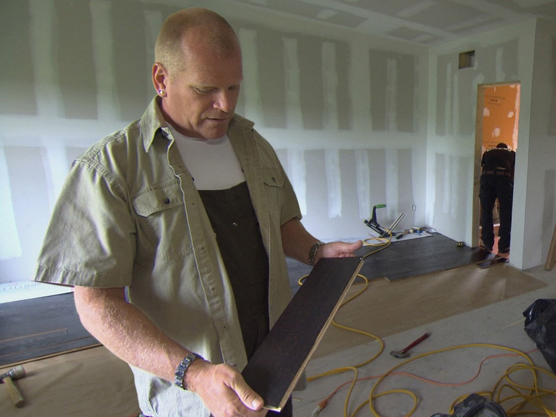 Mike Holmes Inspecting A Piece of Hardwood Flooring