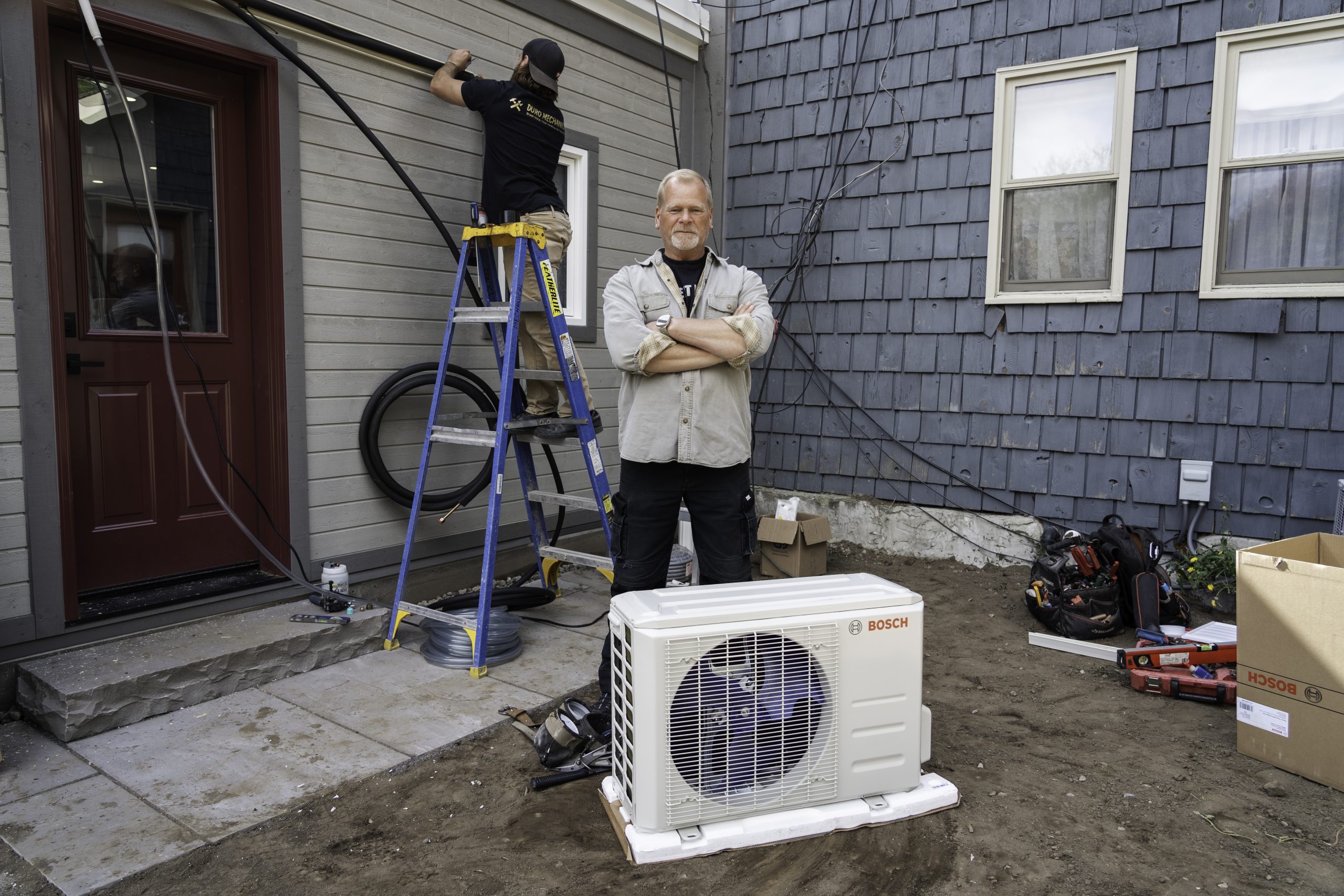Mike Holmes standing in front of a Bosch mini-split heat pump unit, highlighting its use as an efficient ductless heating and cooling solution.